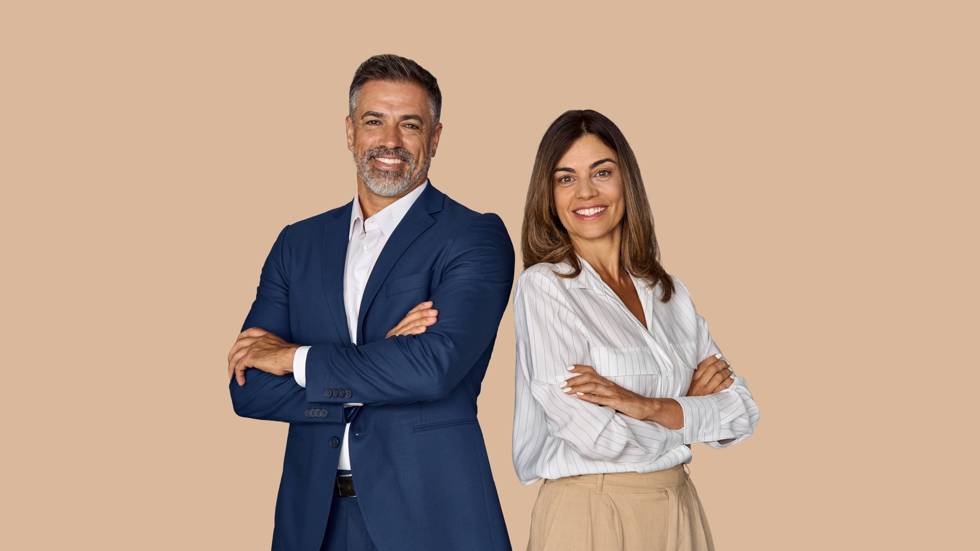 Portrait of two smiling mature Latin business man, European business woman standing arms crossed isolated on beige background. Diverse colleagues, group team of confident professional business people